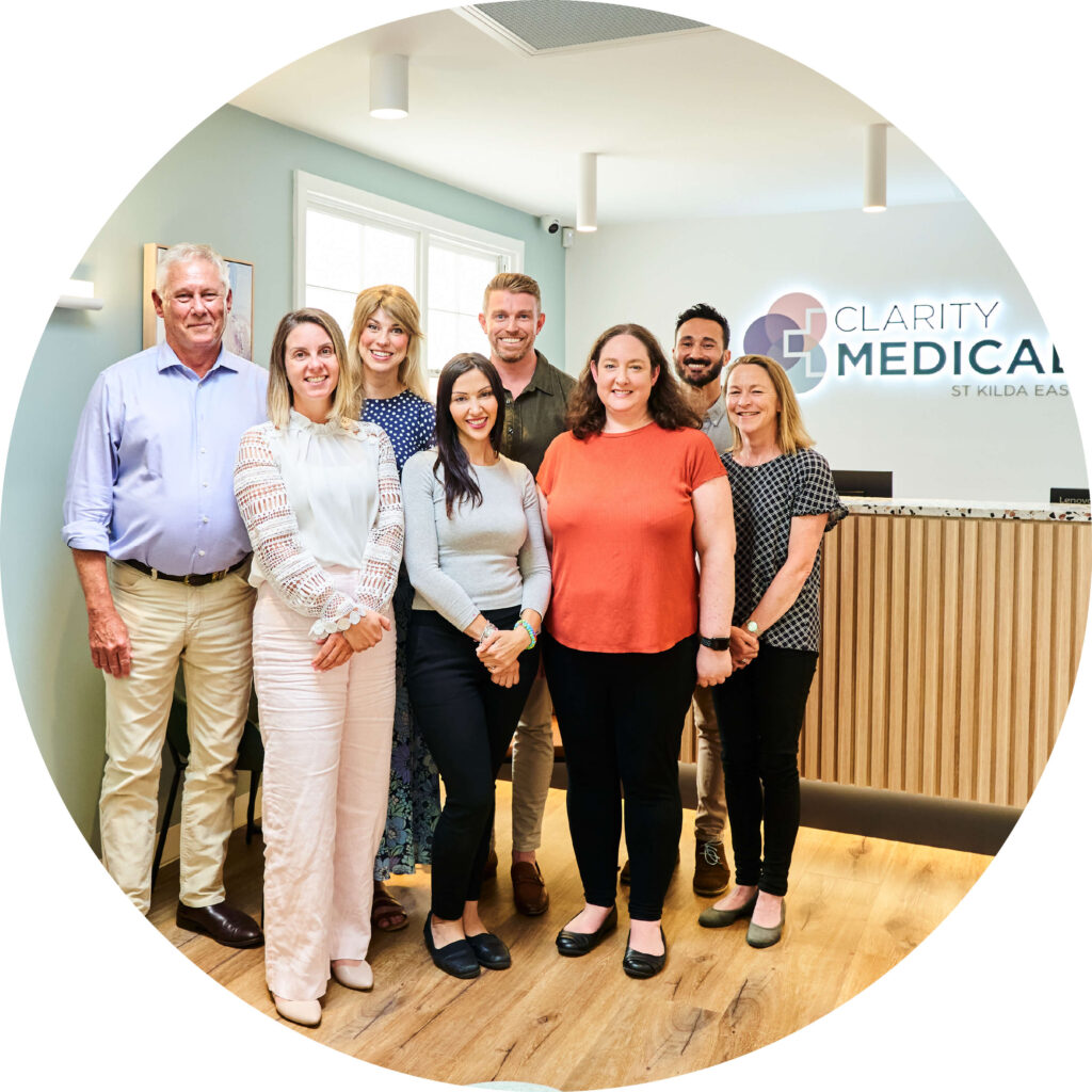 Photo of the team from Clarity Medical St Kilda East, standing in the Reception area with an illuminated sign in the background.